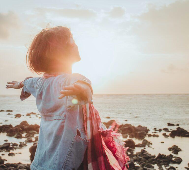 woman on coast with arms open looking at sky