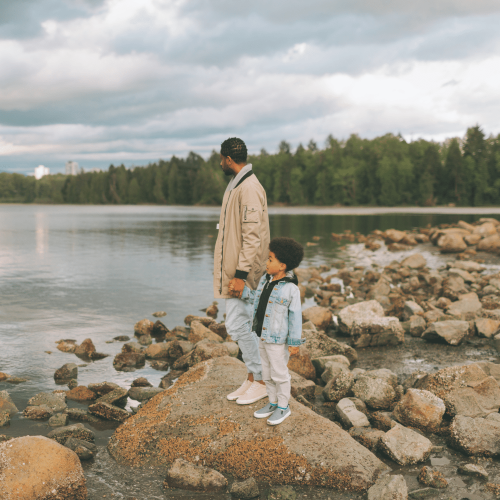 father and son standing on a rock by a lake