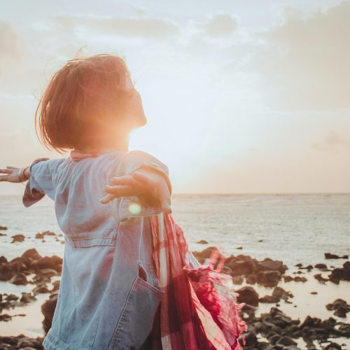 woman on coast with arms open looking at sky